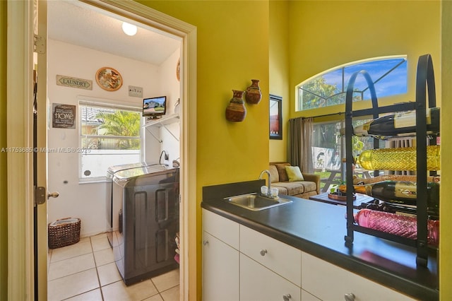 kitchen featuring dark countertops, washer and dryer, white cabinetry, a sink, and light tile patterned flooring