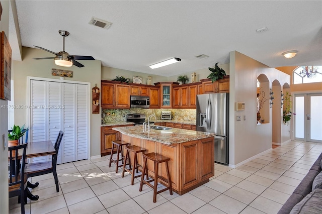 kitchen featuring visible vents, arched walkways, appliances with stainless steel finishes, brown cabinets, and a sink