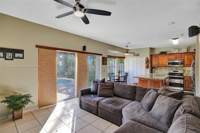 living area with a ceiling fan, a textured ceiling, baseboards, and light tile patterned floors