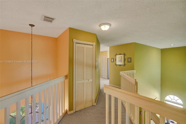 corridor featuring a textured ceiling, visible vents, carpet flooring, and an upstairs landing