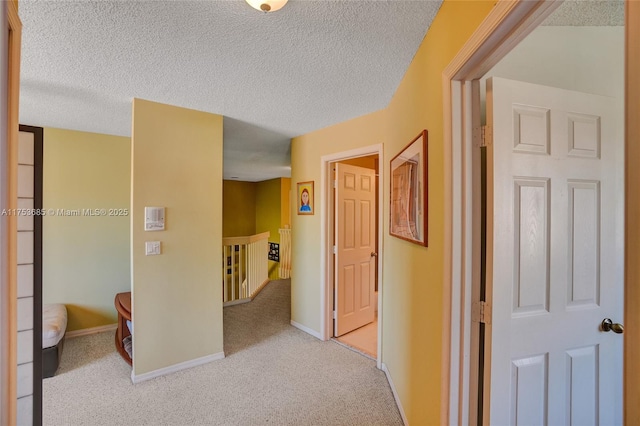 corridor featuring a textured ceiling, baseboards, carpet flooring, and an upstairs landing