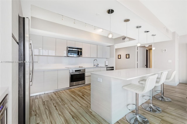 kitchen with appliances with stainless steel finishes, white cabinetry, a sink, modern cabinets, and a kitchen bar