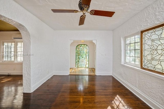 spare room featuring a wall unit AC, arched walkways, wood finished floors, and a textured wall