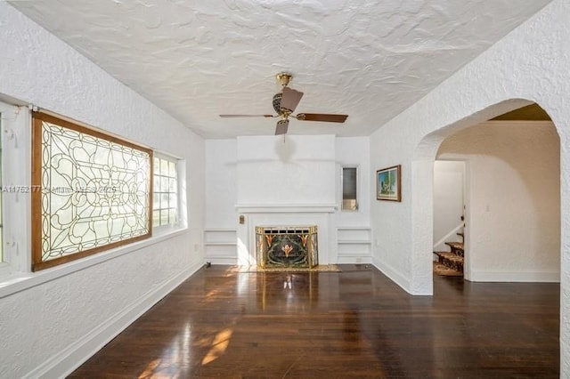 unfurnished living room featuring arched walkways, a textured wall, wood finished floors, and a fireplace with flush hearth