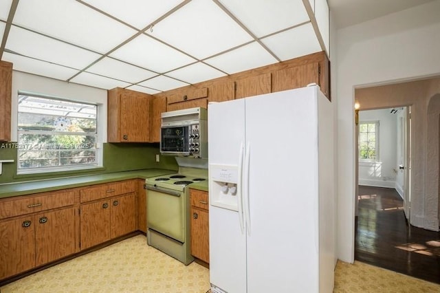 kitchen with light floors, white appliances, brown cabinets, and a drop ceiling