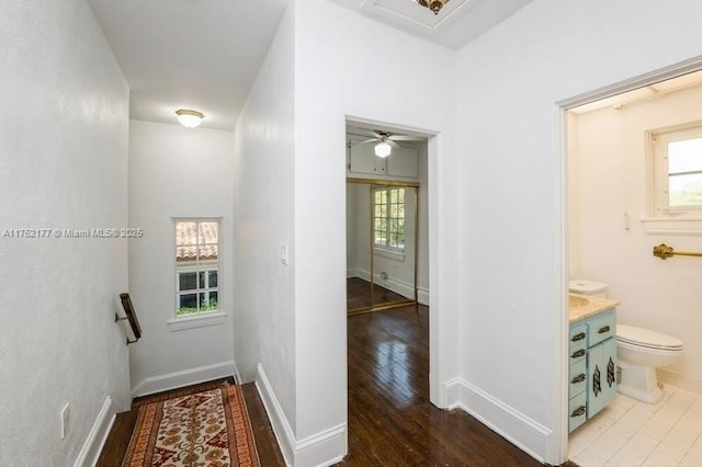 hallway featuring baseboards, wood finished floors, and an upstairs landing