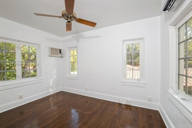 empty room featuring a wall unit AC, baseboards, and wood finished floors