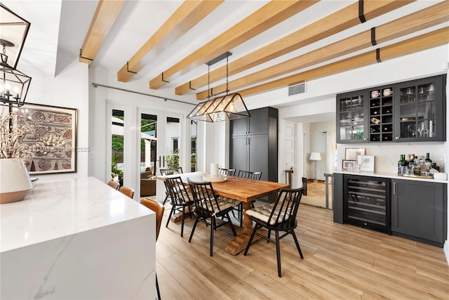 dining area with wine cooler, beamed ceiling, a dry bar, and light wood finished floors