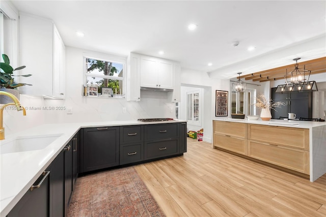 kitchen with stainless steel gas cooktop, a sink, white cabinets, backsplash, and light wood finished floors