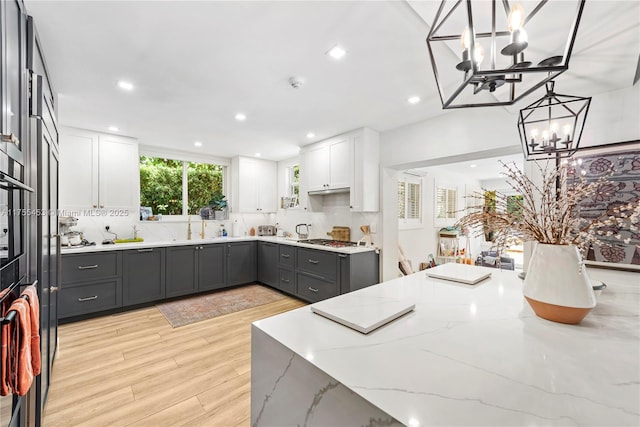 kitchen with stainless steel gas cooktop, light stone counters, gray cabinets, and white cabinetry