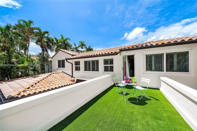 back of house with a lawn, a tiled roof, and stucco siding