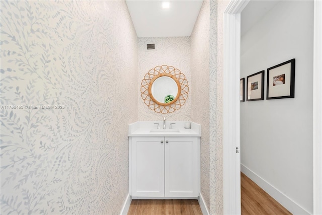 bathroom with wallpapered walls, wood finished floors, vanity, and baseboards