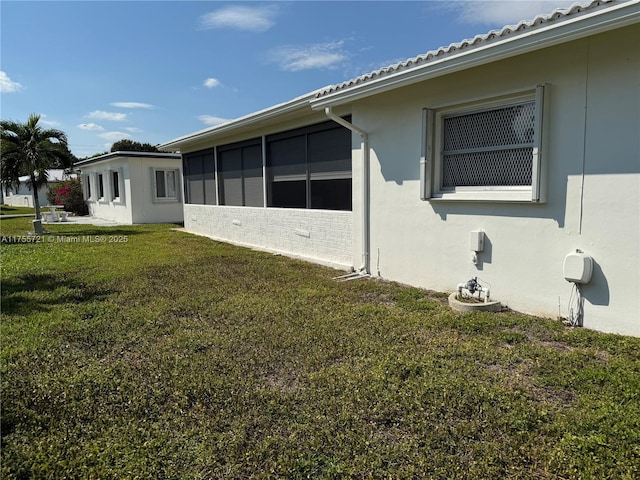 view of side of home with a sunroom, a lawn, and stucco siding