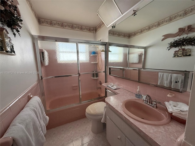 bathroom featuring toilet, enclosed tub / shower combo, tile walls, and vanity