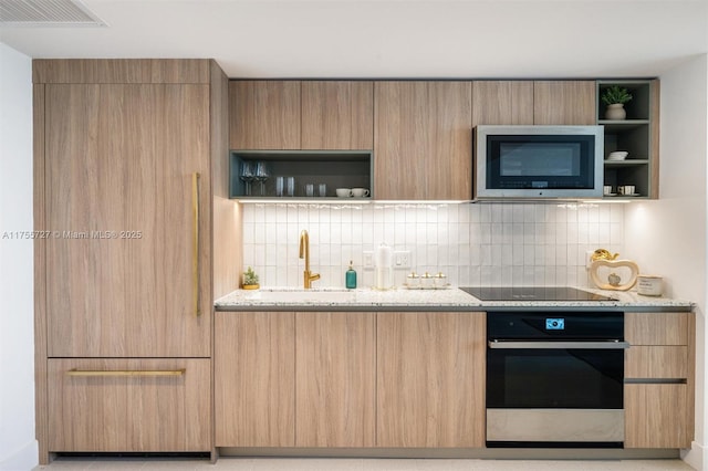 kitchen with tasteful backsplash, black electric cooktop, stainless steel oven, open shelves, and a sink