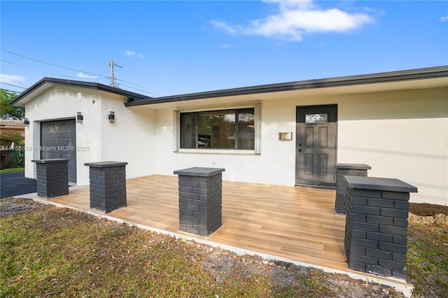 property entrance featuring a garage, a wooden deck, and stucco siding