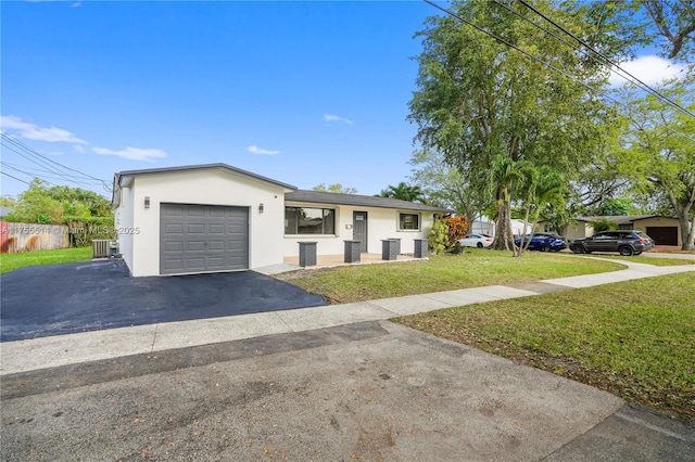 ranch-style house featuring driveway, an attached garage, central air condition unit, a front yard, and stucco siding