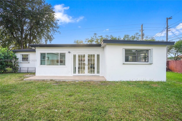 rear view of house featuring stucco siding, fence, a lawn, and french doors