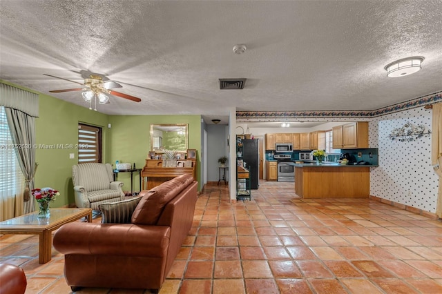 living area with light tile patterned floors, visible vents, a ceiling fan, a textured ceiling, and baseboards