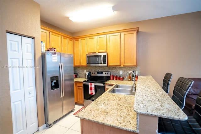 kitchen with appliances with stainless steel finishes, a peninsula, a sink, backsplash, and light tile patterned flooring