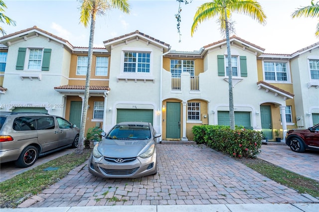 multi unit property featuring decorative driveway, a tile roof, an attached garage, and stucco siding