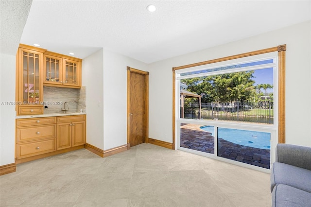 interior space featuring light countertops, decorative backsplash, glass insert cabinets, a sink, and baseboards