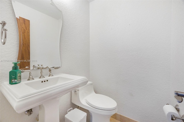 bathroom with a sink, a textured wall, and toilet