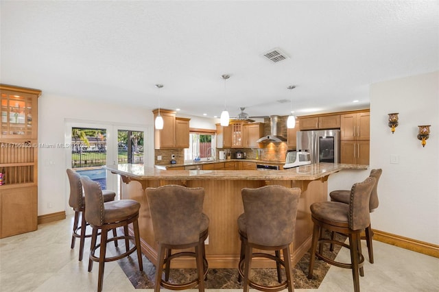 kitchen featuring wall chimney exhaust hood, tasteful backsplash, visible vents, a sink, and stainless steel fridge with ice dispenser