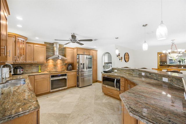 kitchen with stainless steel appliances, decorative backsplash, a sink, dark stone countertops, and wall chimney exhaust hood