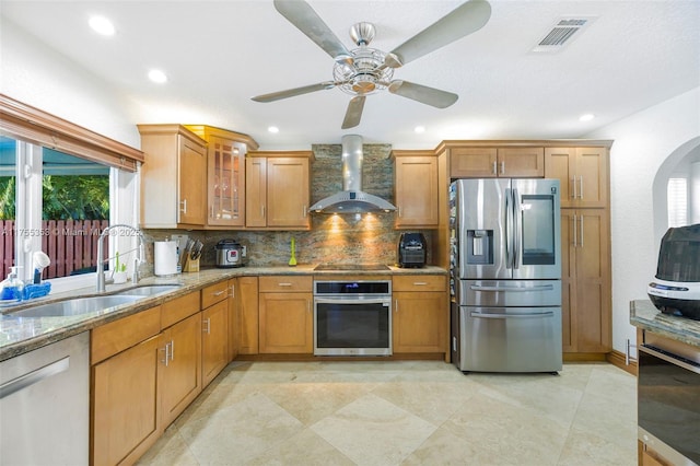 kitchen featuring stainless steel appliances, visible vents, a sink, wall chimney range hood, and light stone countertops