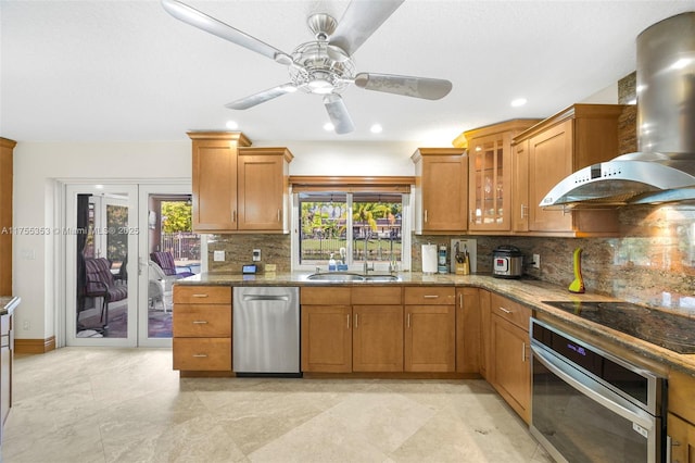 kitchen featuring stainless steel appliances, wall chimney range hood, brown cabinetry, and a sink