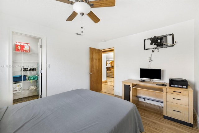 bedroom featuring light wood finished floors, visible vents, ceiling fan, a walk in closet, and a closet
