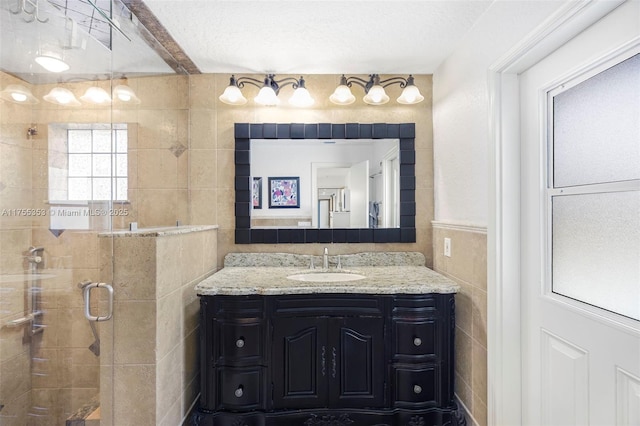 bathroom with a textured ceiling, a stall shower, vanity, and tile walls