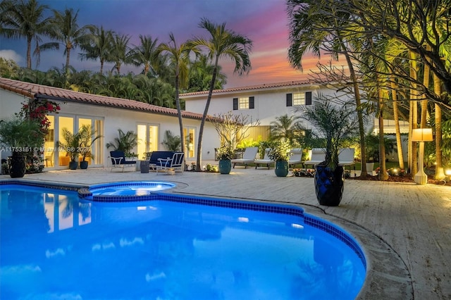 pool at dusk featuring a patio area, french doors, and a pool with connected hot tub