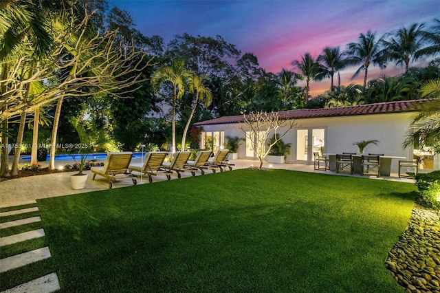 yard at dusk with a patio area, an outdoor pool, and french doors