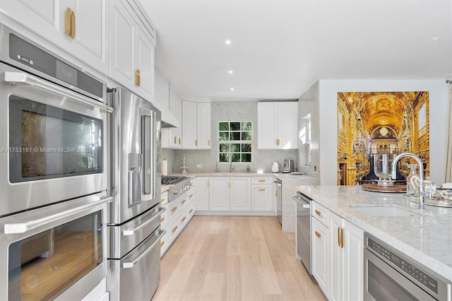 kitchen featuring tasteful backsplash, light stone countertops, stainless steel appliances, white cabinetry, and a sink