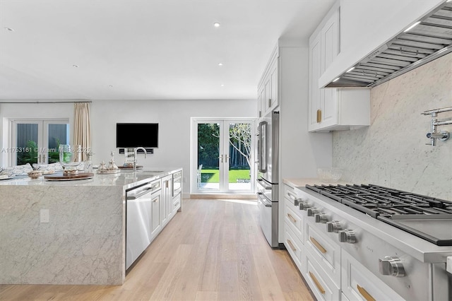 kitchen featuring wall chimney range hood, light stone counters, appliances with stainless steel finishes, french doors, and white cabinets