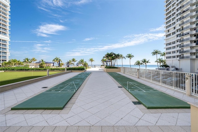 surrounding community featuring fence, a view of the beach, shuffleboard, and a water view