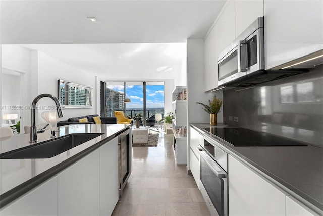 kitchen featuring tasteful backsplash, white cabinets, appliances with stainless steel finishes, floor to ceiling windows, and a sink