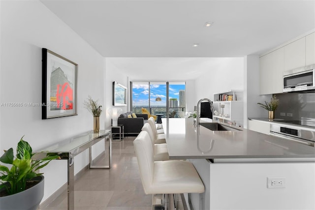 68 SE 6th St Unit 3506, Miami, FL 33131 - kitchen featuring stainless steel microwave, white cabinets, a sink, modern cabinets, and a kitchen breakfast bar