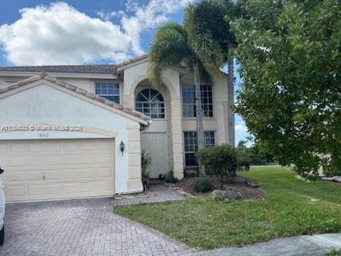 view of front of home featuring decorative driveway, a tile roof, stucco siding, an attached garage, and a front yard