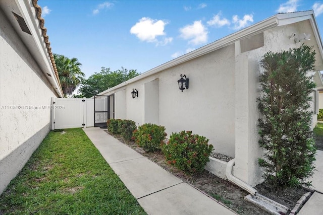 exterior space featuring a yard, a gate, fence, and stucco siding