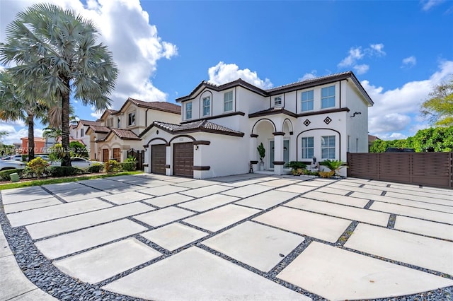 mediterranean / spanish-style house with a tile roof, stucco siding, concrete driveway, fence, and a garage