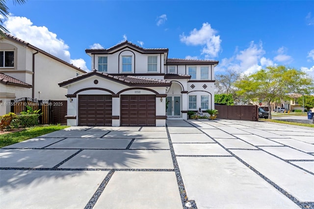 mediterranean / spanish home with a tiled roof, fence, concrete driveway, and stucco siding