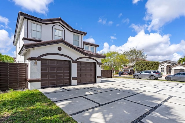 mediterranean / spanish-style house with concrete driveway, a tiled roof, an attached garage, fence, and stucco siding