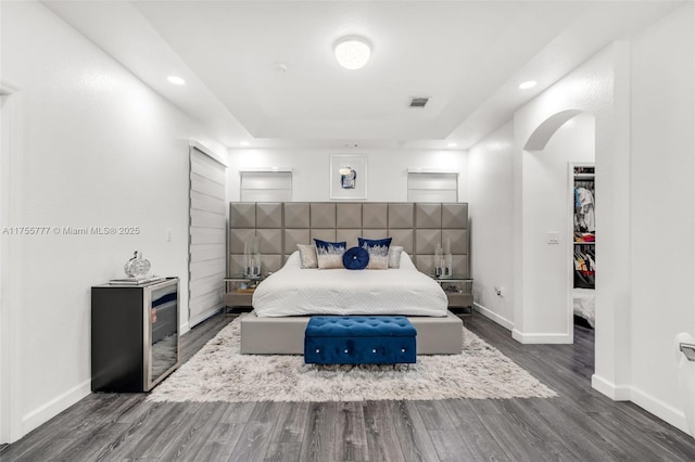 bedroom featuring baseboards, visible vents, arched walkways, wood finished floors, and a walk in closet