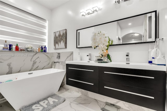 bathroom with marble finish floor, a sink, a freestanding bath, and double vanity