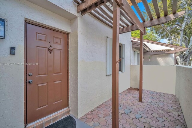 property entrance with a pergola, a patio, and stucco siding