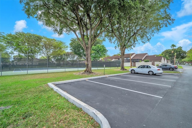 uncovered parking lot with a tennis court and fence