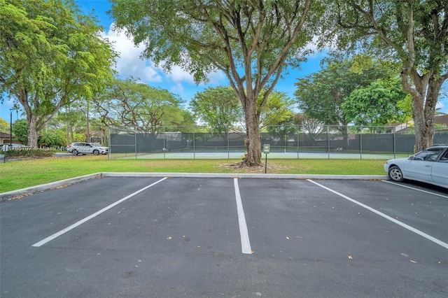 uncovered parking lot featuring a tennis court and fence